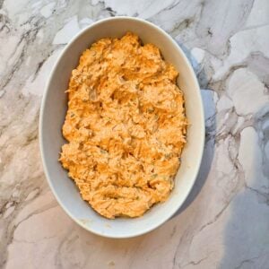 Buffalo chicken dip ready to bake in an oval baking dish.
