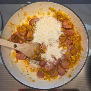 Uncooked white rice being stirred into the sausage and veggie mixture.