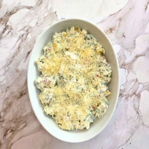 Topping the spinach artichoke dip with shredded cheese before baking.