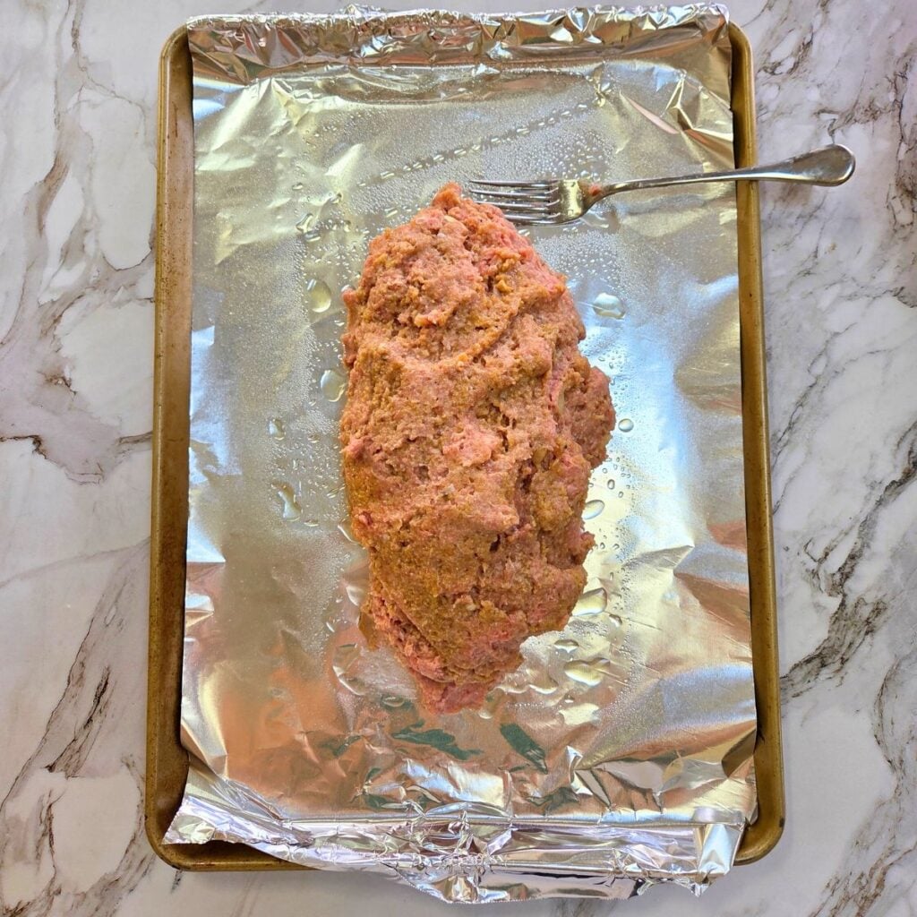 Uncooked ground turkey meatloaf on a foil covered baking sheet.