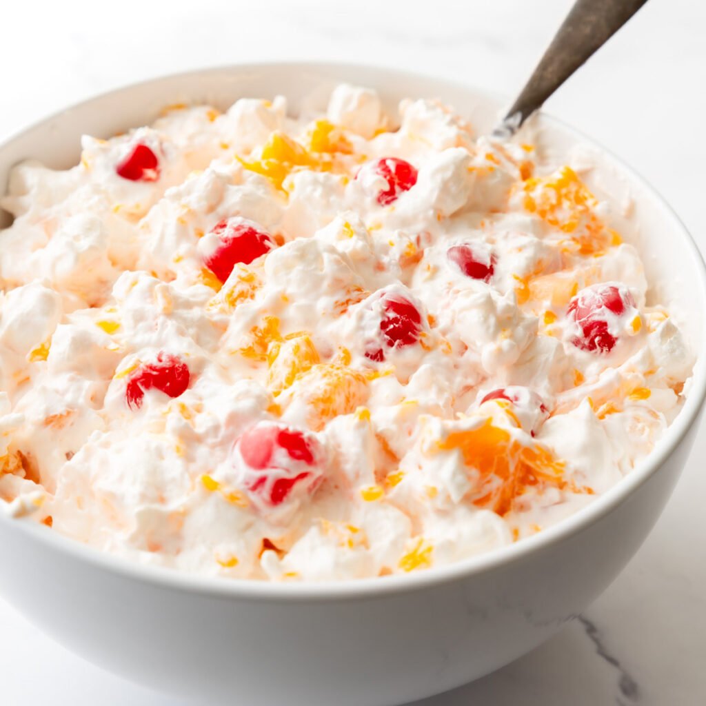 Large serving bowl of Ambrosia fruit salad with a spoon resting in it.