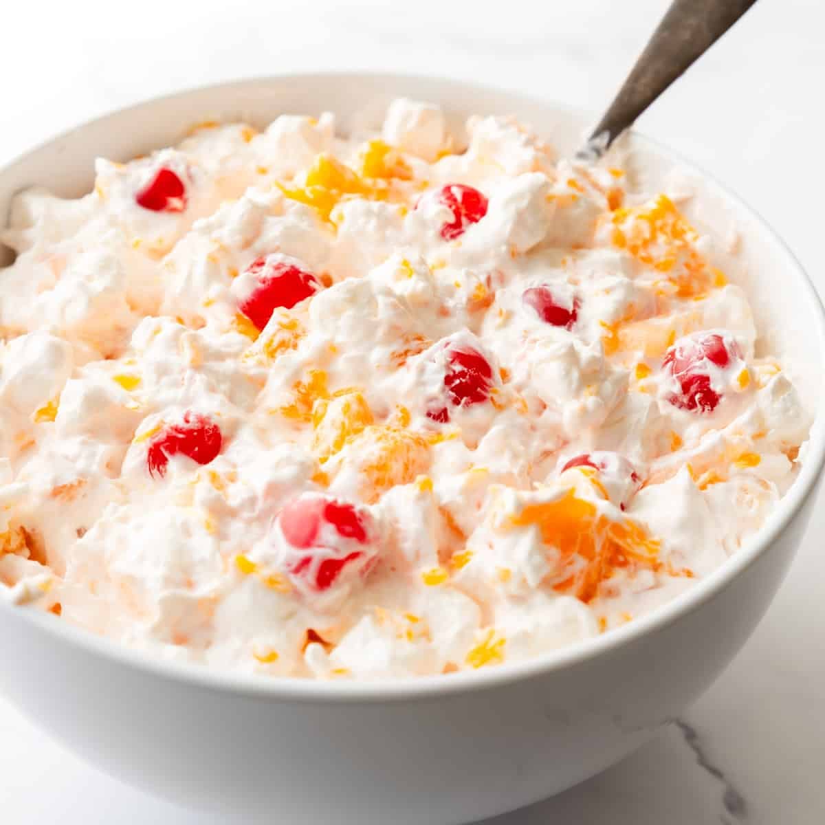 Large serving bowl of Ambrosia fruit salad with a spoon resting in it.