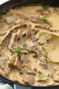 Close up of beef stroganoff with large beef steak pieces in a creamy rich mixture.