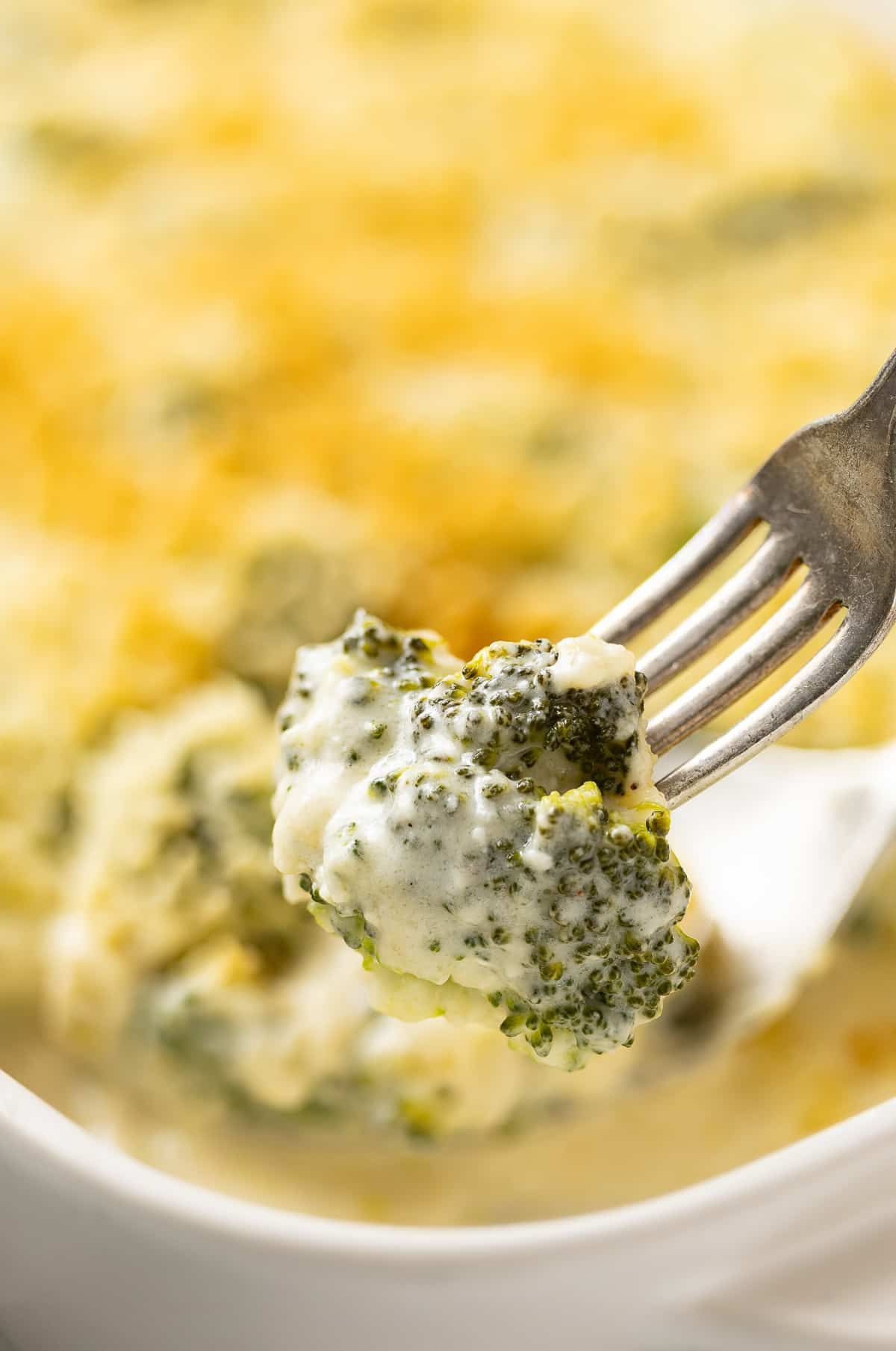 Fork holding up a broccoli floret coated in a homemade cheese sauce.
