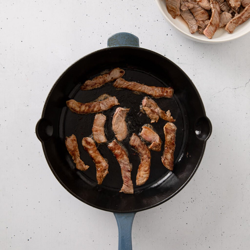Steak slices frying in a skillet.