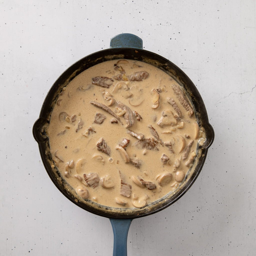 Steak pieces added to a stroganoff mixture in a skillet.