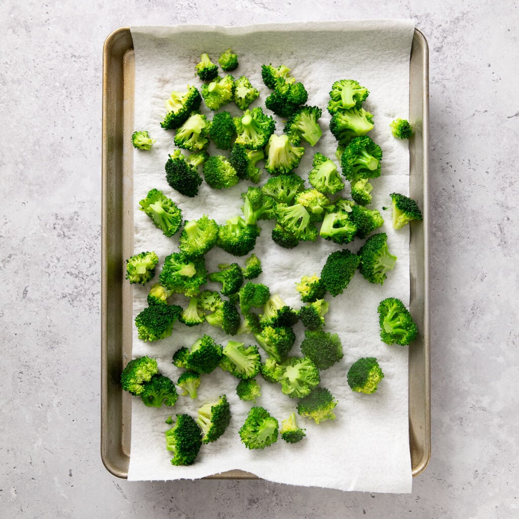 Clean, raw broccoli florets drying on a paper towel lined baking sheet.