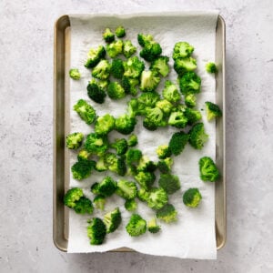 Clean, raw broccoli florets drying on a paper towel lined baking sheet.