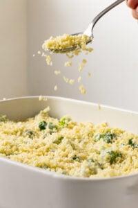 Breadcrumbs being sprinkled over cheese coated broccoli florets.