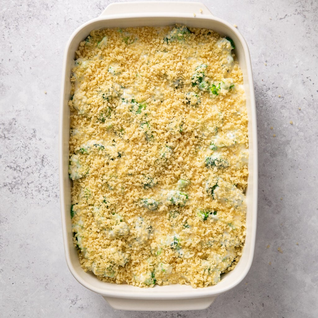 Top view of panko breadcrumbs topping the cheese covered broccoli florets in a baking dish, ready to bake.