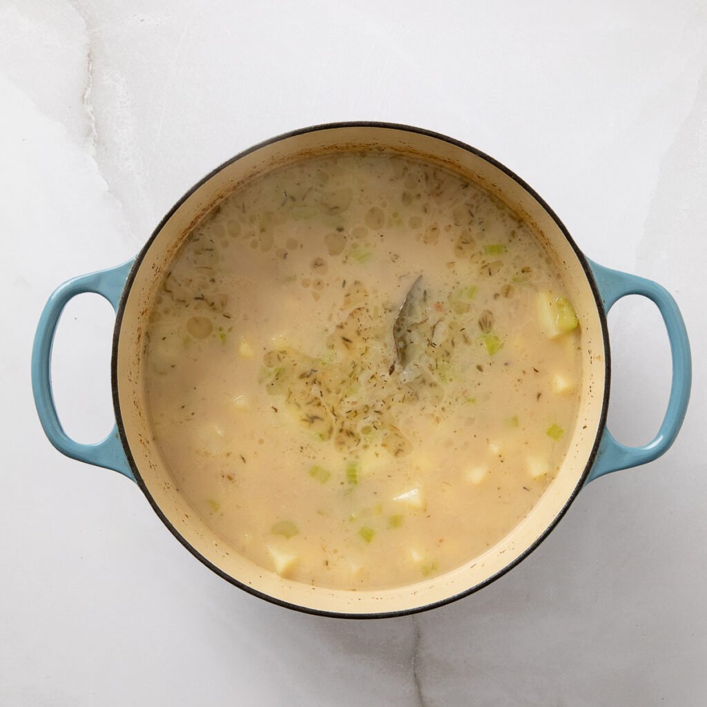 Clam chowder ingredients added to a Dutch oven.