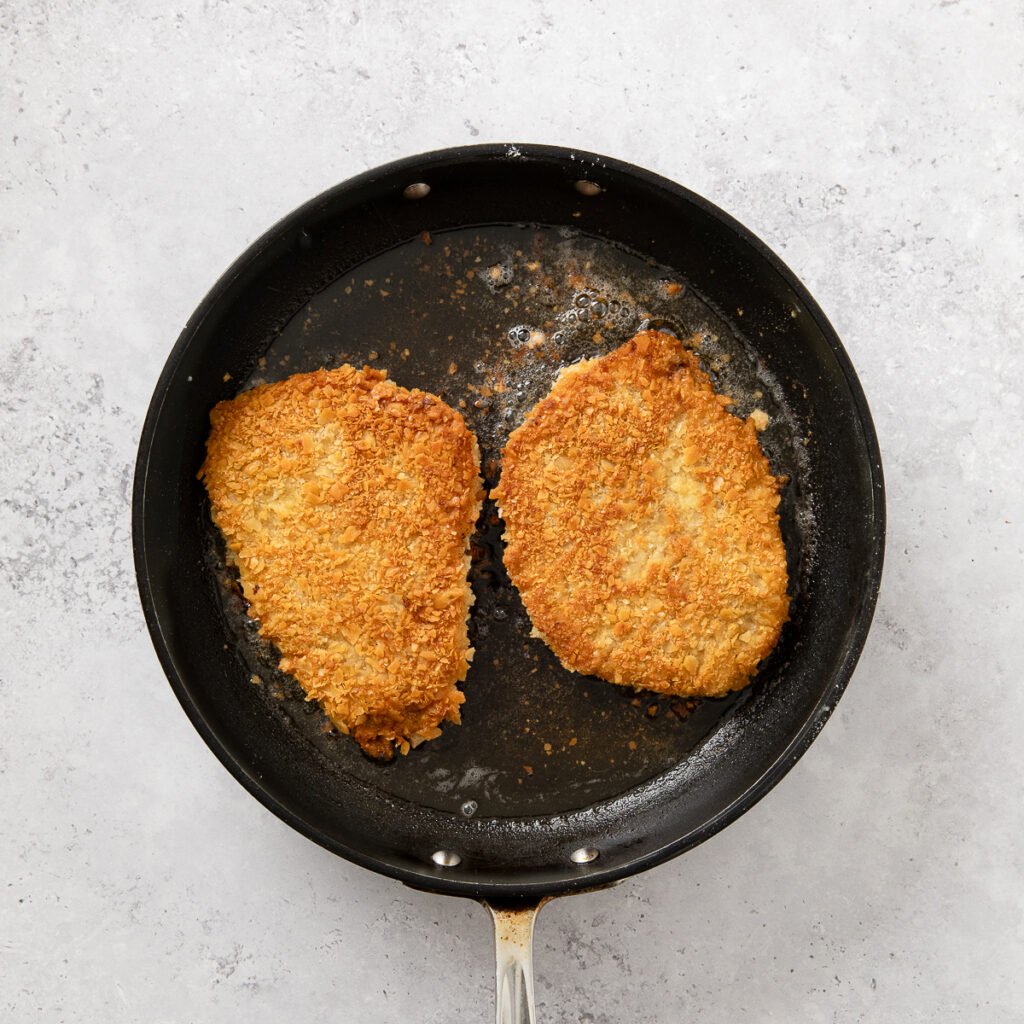 Cubed steak frying in a skillet with a crunchy saltine texture coating it.