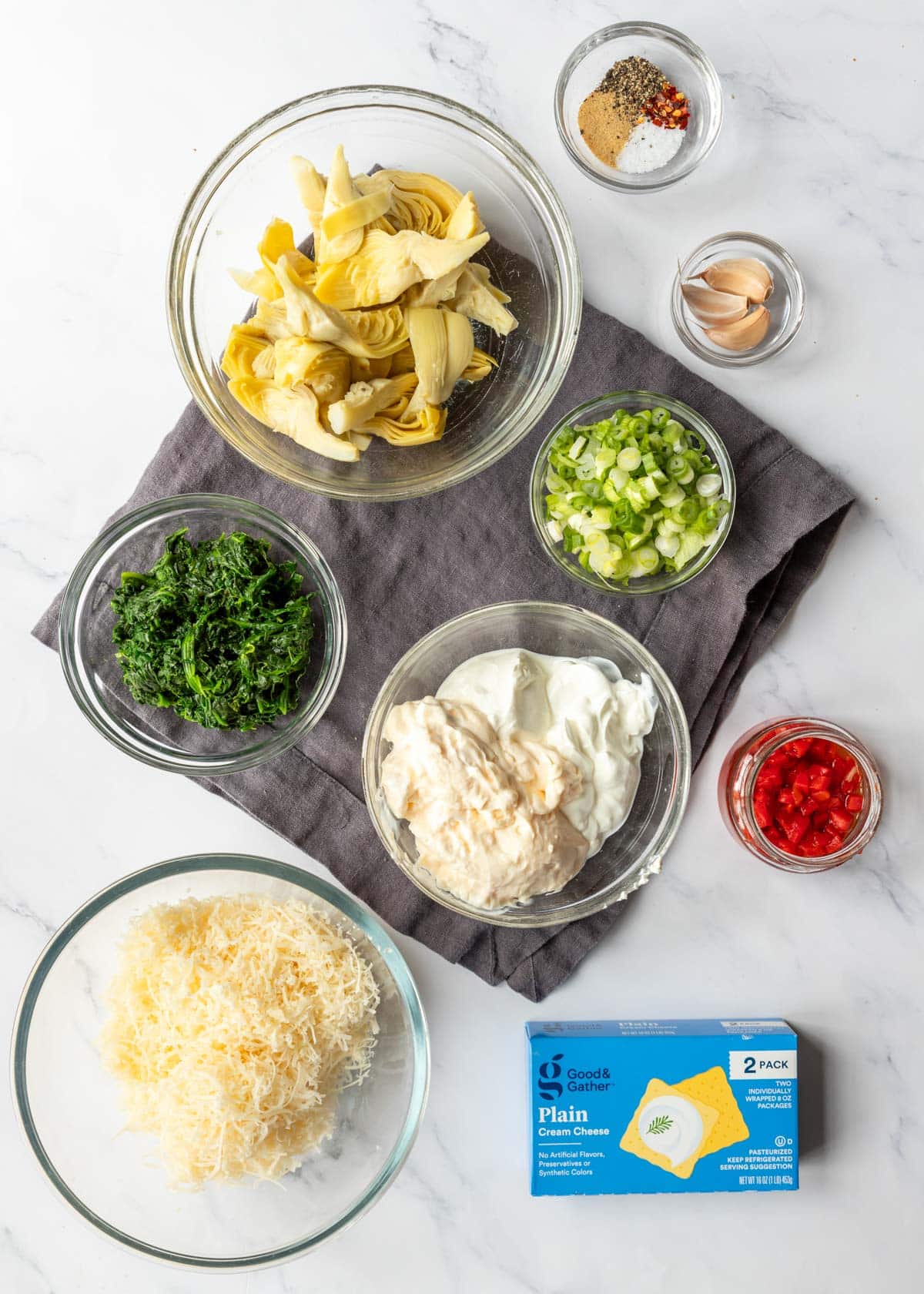 Ingredients measured out and shown in small dishes to prepare spinach artichoke dip.