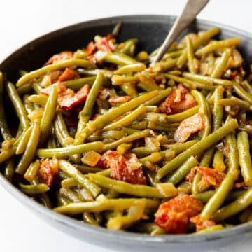 Crispy bacon pieces mixed in with green beans in a skillet.