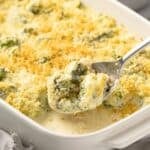 Scoop of broccoli cheese casserole coming out of a baking dish.