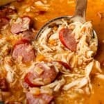 Close of up of shredded chicken, sausage slices and rice in a hearty gumbo broth.