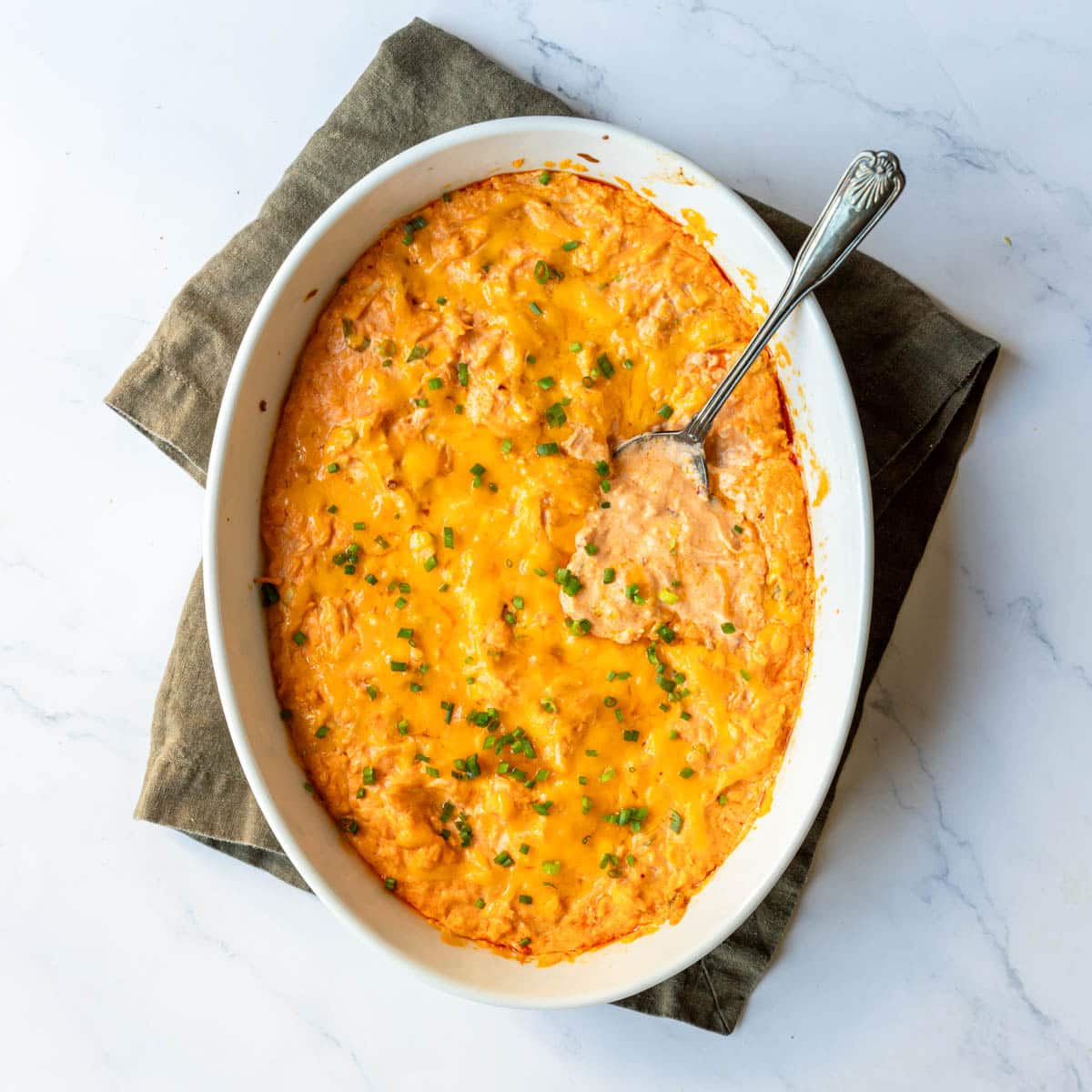 Top view of a spoon resting in the hot bubbly buffalo chicken dip served as an appetizer.
