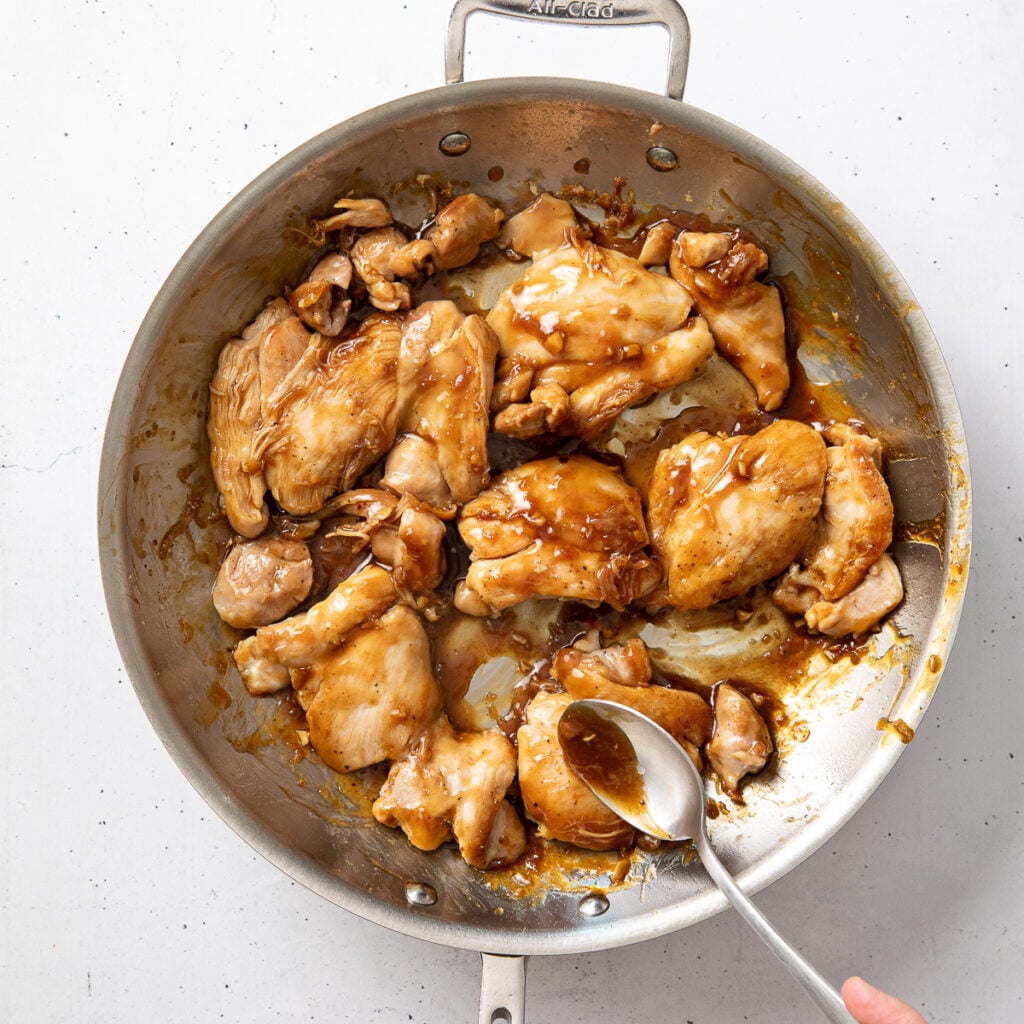 Spoon adding teriyaki sauce over cooked chicken thighs.