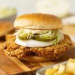 Close up of a fresh made fried pork tenderloin sandwich topped with onion rings, pickles, horseradish mayo and lettuce.