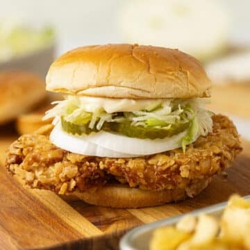 Close up of a fresh made fried pork tenderloin sandwich topped with onion rings, pickles, horseradish mayo and lettuce.