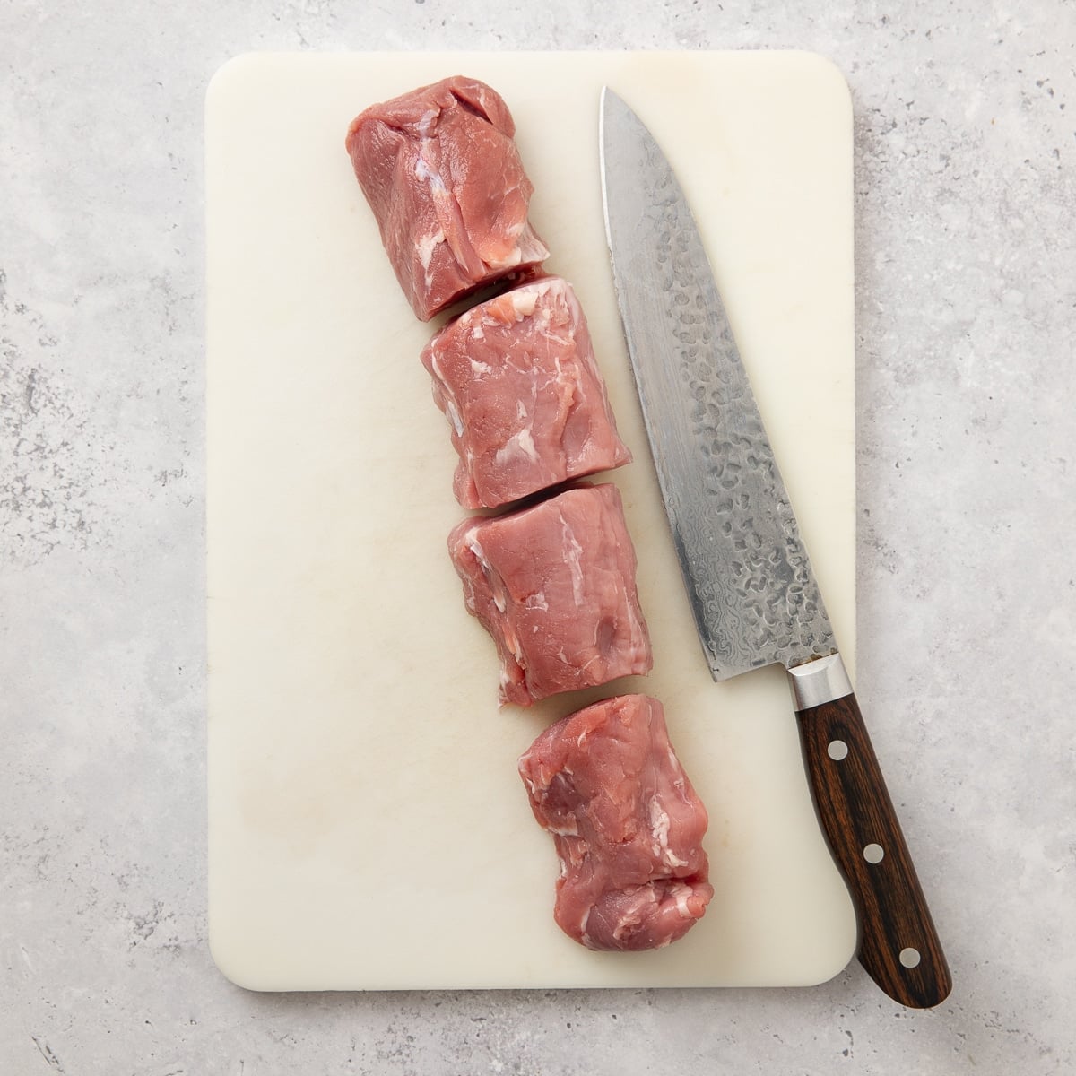 Raw pork tenderloin cut into large chunks on a cutting board.