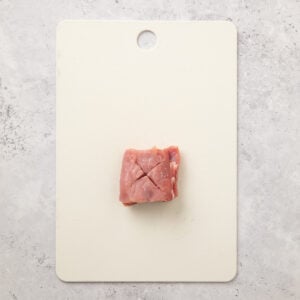 An X cut into a chunk of pork tenderloin on a cutting board before frying.