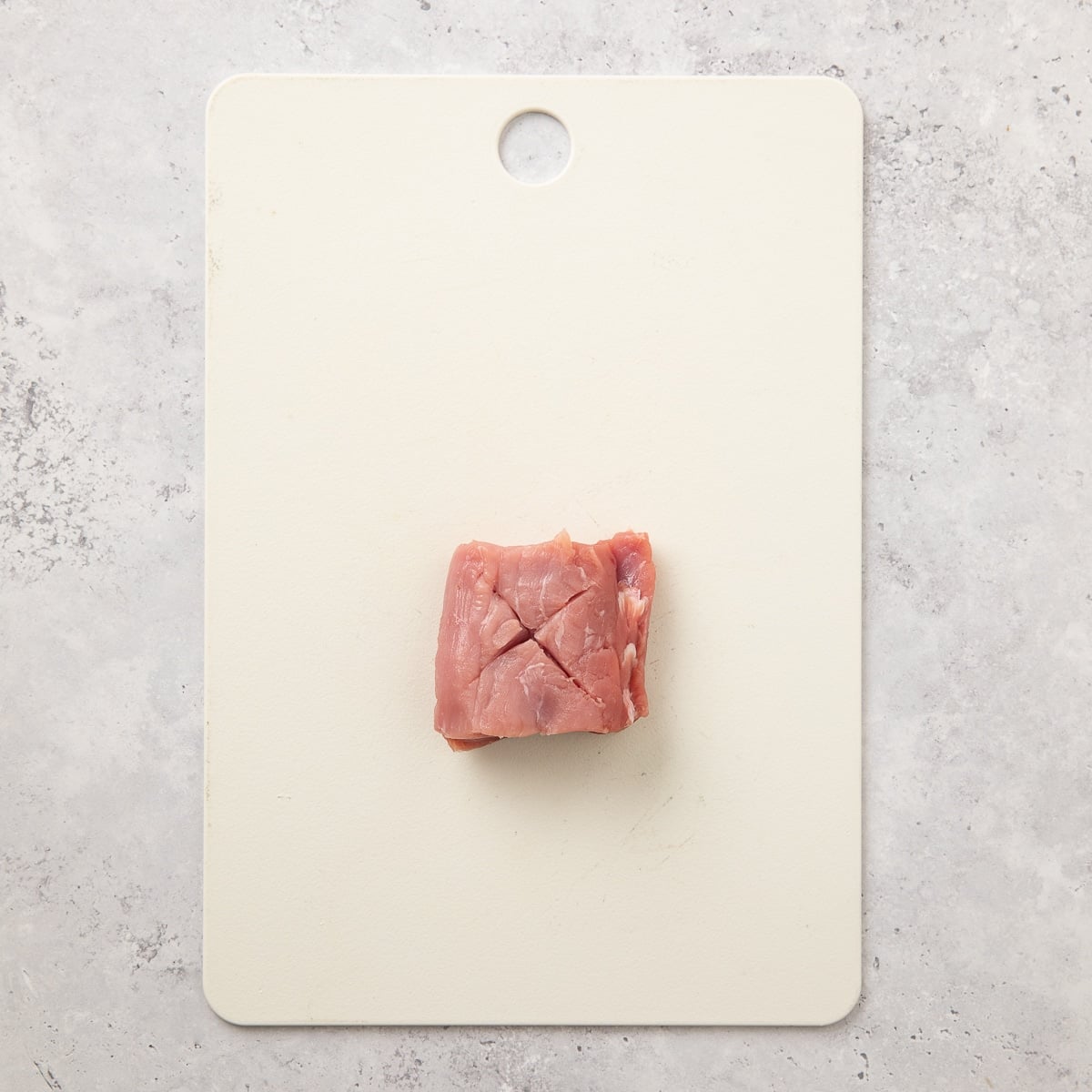 An X cut into a chunk of pork tenderloin on a cutting board before frying.