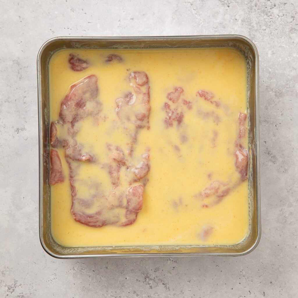 Raw pork tenderloin resting in an egg mixture.