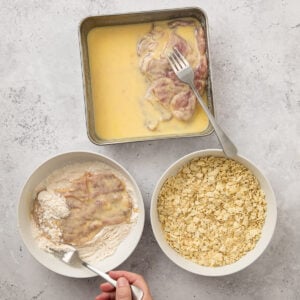 Process shot of thin pork pieces in an egg mixture, then dredged in flour mixture with the Ritz crackers ready to be topped over the pork.