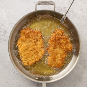 Pork tenderloin pieces frying in a skillet.