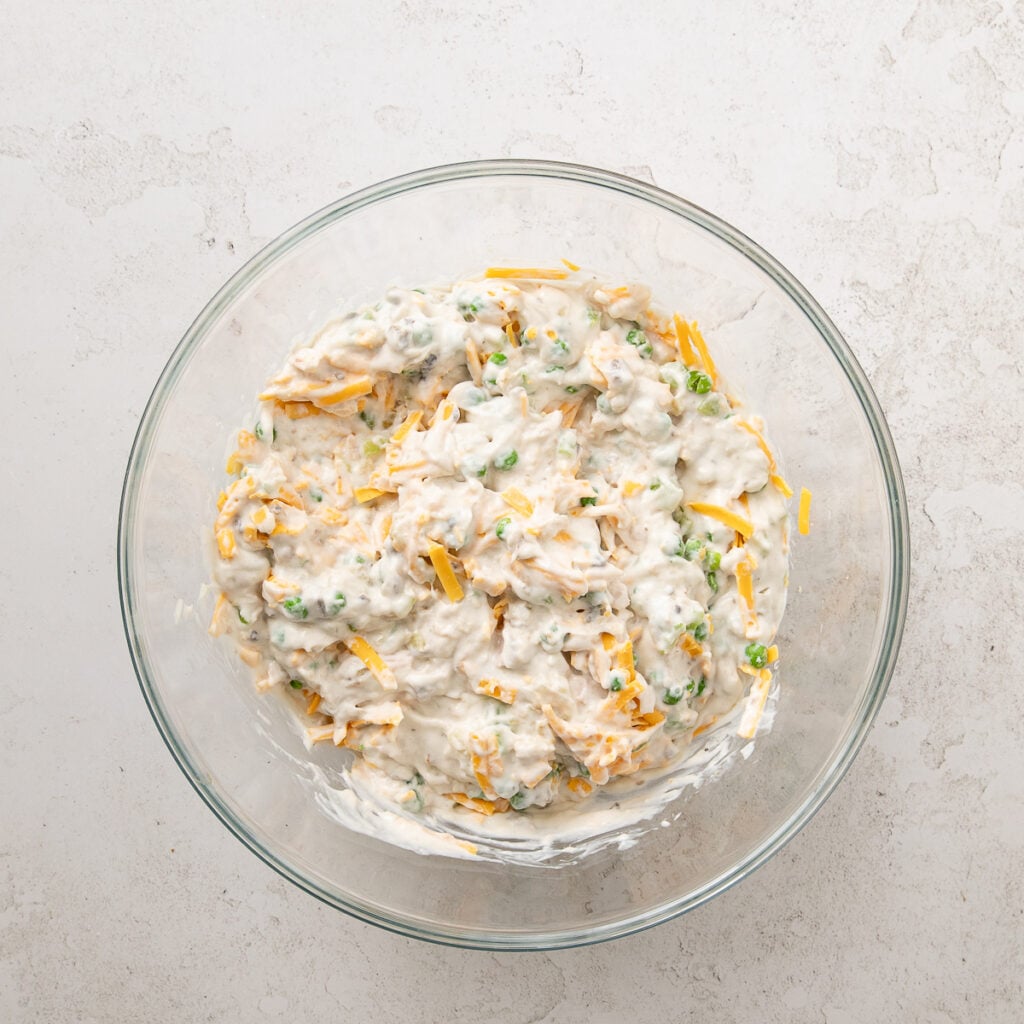 Shredded cheese added to tuna mixture in a glass bowl.