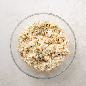 Top view of a bowl of tuna mixture coating wide egg noodles combined in a glass bowl.