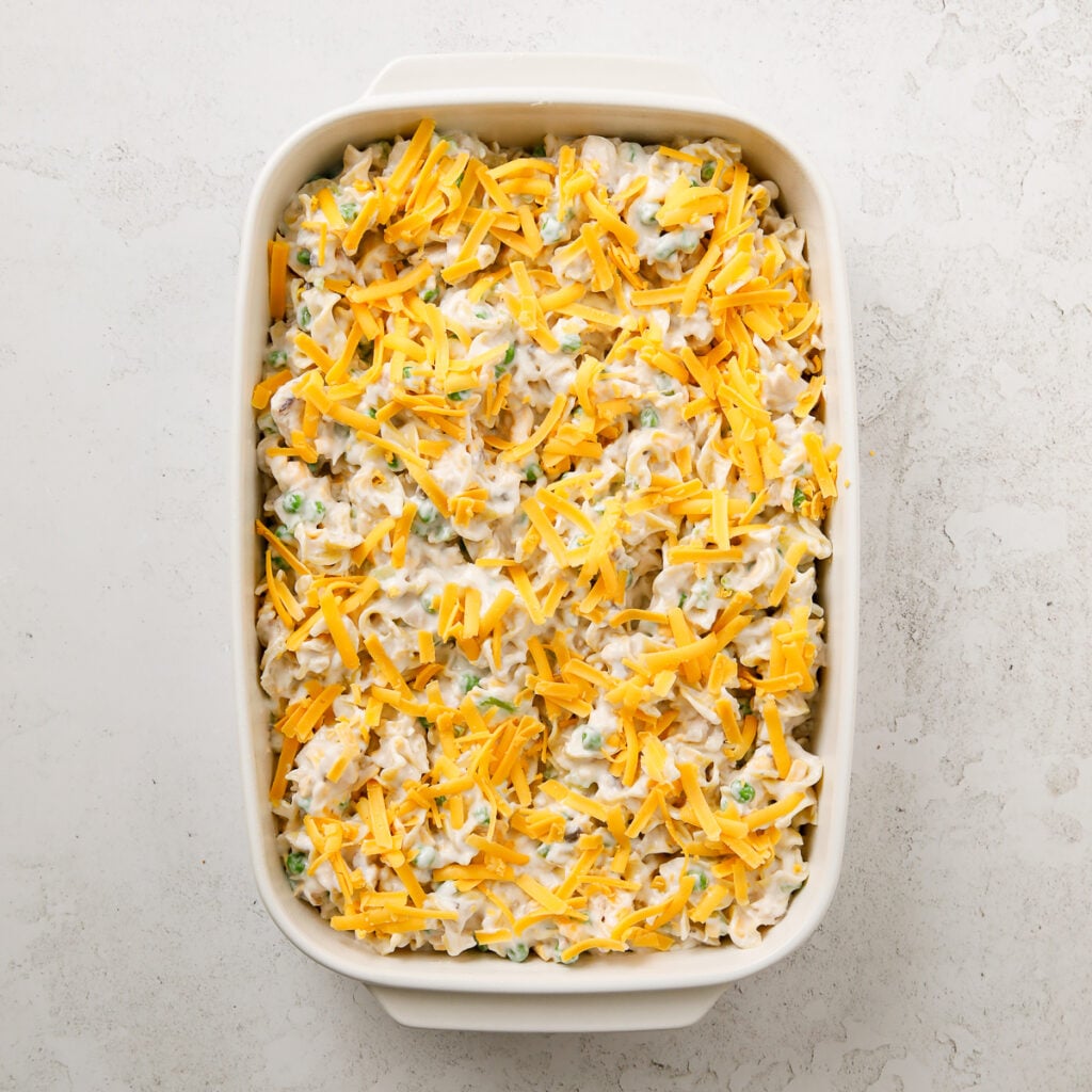 Shredded cheese sprinkled over tuna noodle casserole in a baking dish.
