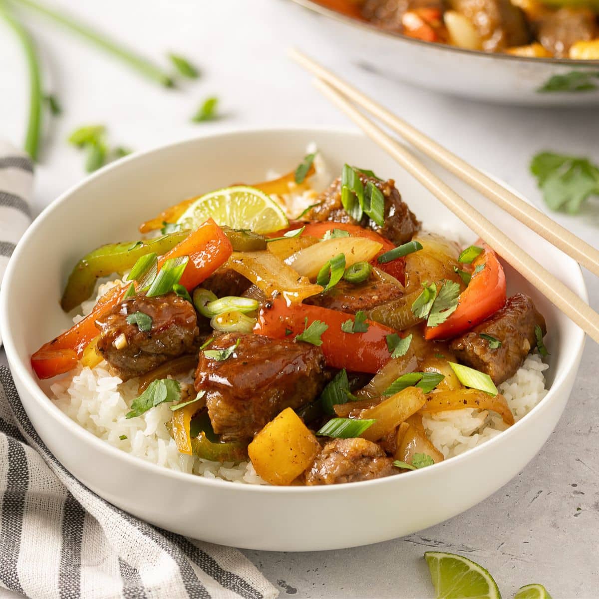 a bowl of sweet and sour beef over rice with chop sticks to the side