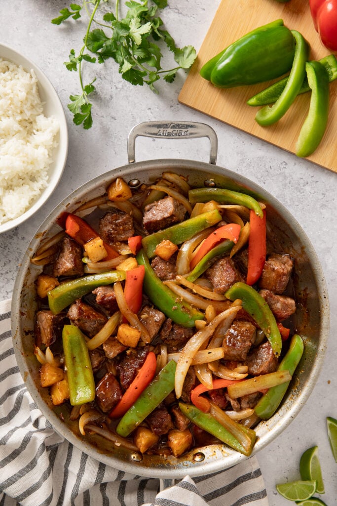 sweet and sour beef made in a skillet with a bowl of cooked rice to the side