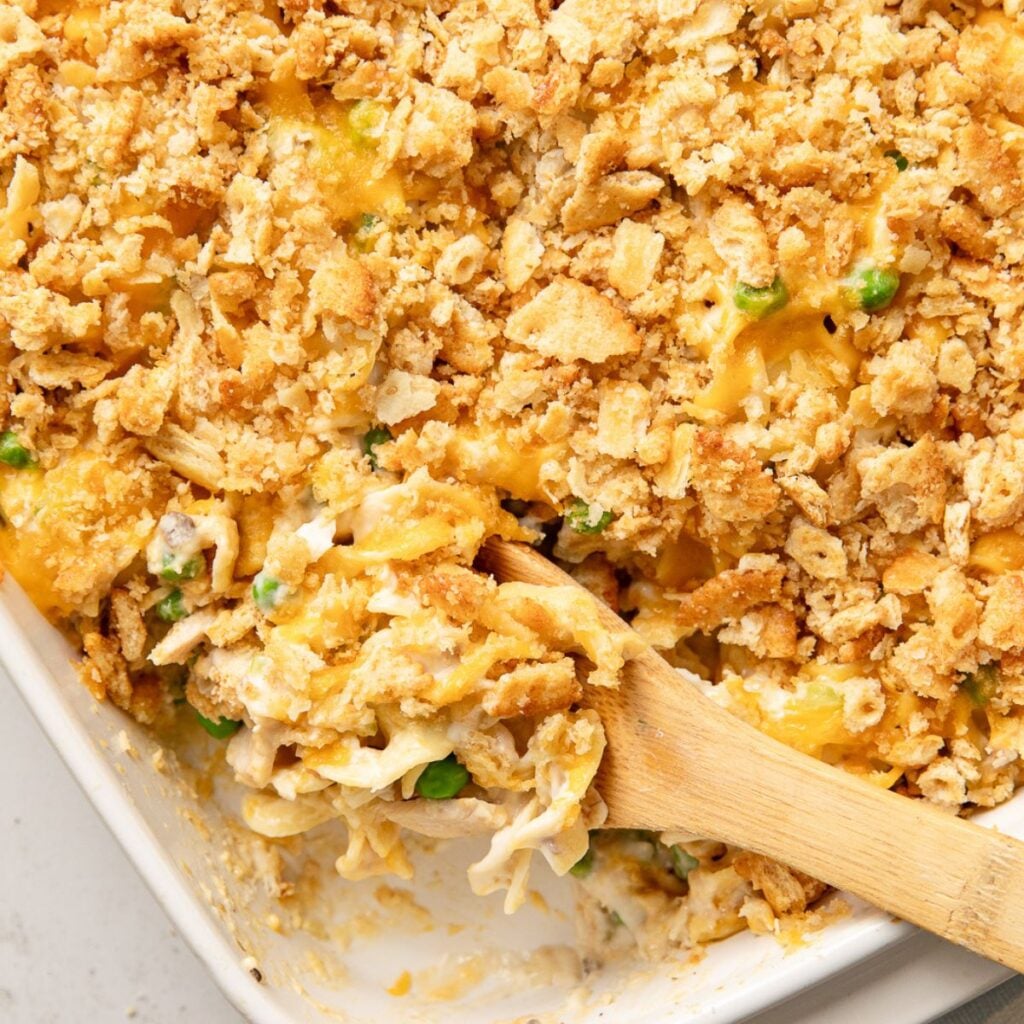 Wooden spoon resting in a baking dish of tuna noodle casserole.