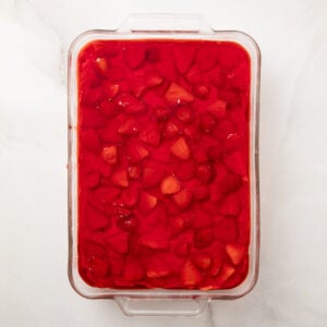 Strawberry mixture added to the top of the cream cheese mixture and pretzel crust in a glass baking pan.