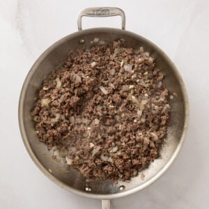 Skillet with cooked ground beef and chopped onions.