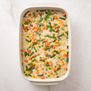 Gravy, ground beef and mixed veggies in a baking dish.