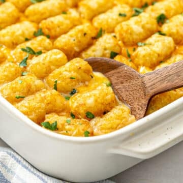 Wooden spoon in a baking dish of tater tot casserole.